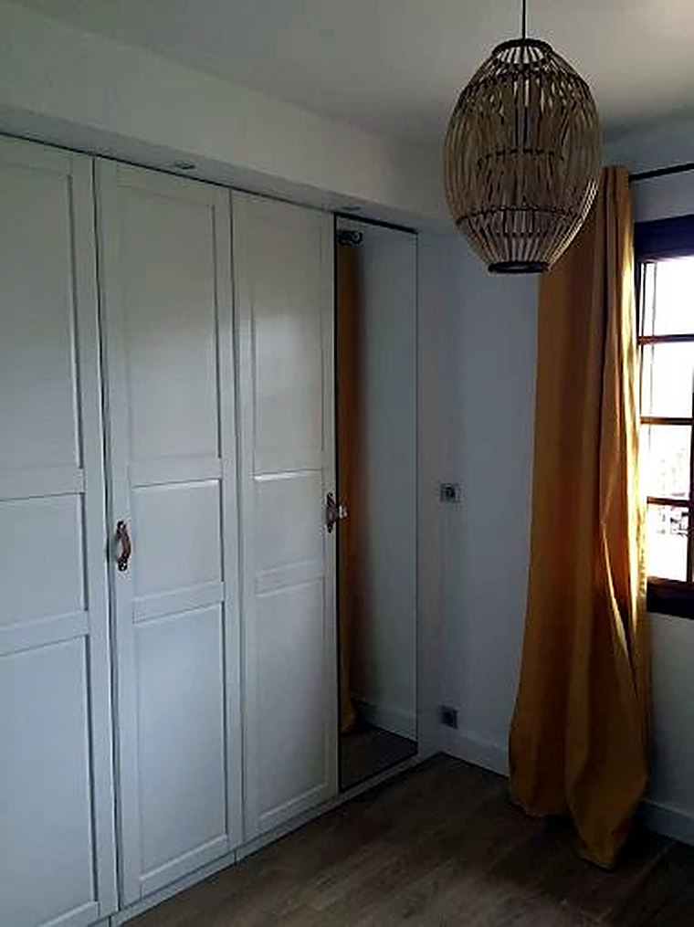 Chambre avec armoire blanche à miroir et suspension en rotin